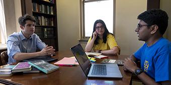 three Honors College students meet to study together at a table with books, notebooks, and laptops. 