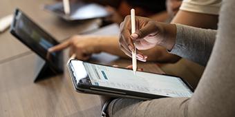 A student holds a stylus over a digital tablet while reviewing information.